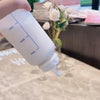A white frosted water bottle with volume markings is held by a hand, set against a blurred background.