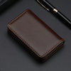 A dark brown stitched PU leather card holder wallet resting on a dark surface next to a black pen.