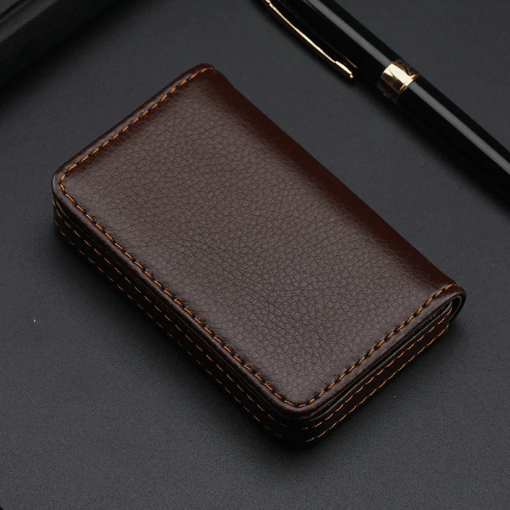 A dark brown stitched PU leather card holder wallet resting on a dark surface next to a black pen.