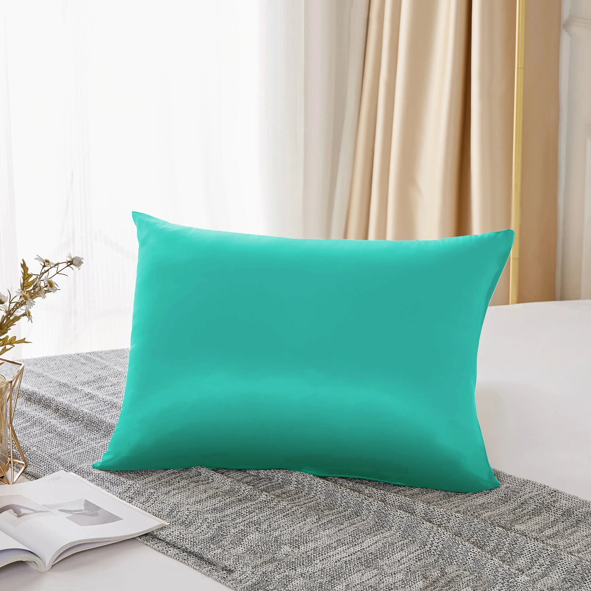 Housse de couette en soie bleu sarcelle posée sur un tissu gris texturé près d'une fenêtre avec des rideaux transparents.