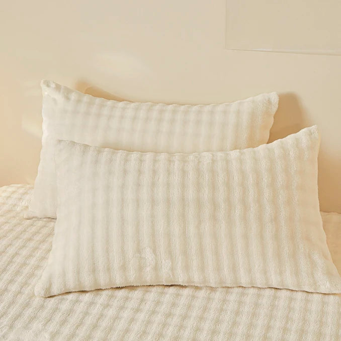 White cozy faux fur fitted sheet with vertical ribbing resting on a light-colored bed.