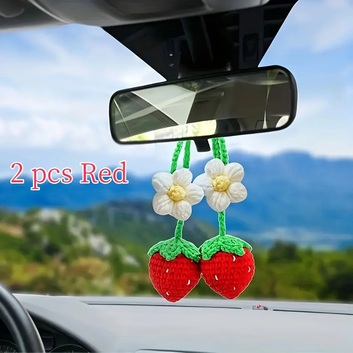 Two red crochet strawberry pendants hanging from a mirror on a car windshield.