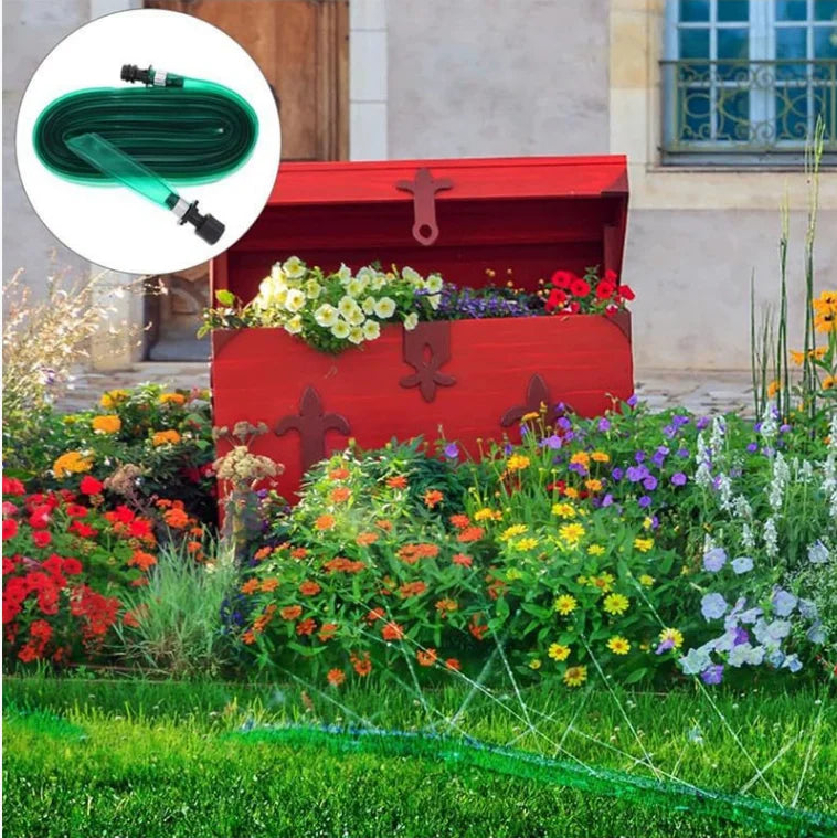 A red planter box filled with flowers sits in a garden setting, with a green hose visible in the foreground.