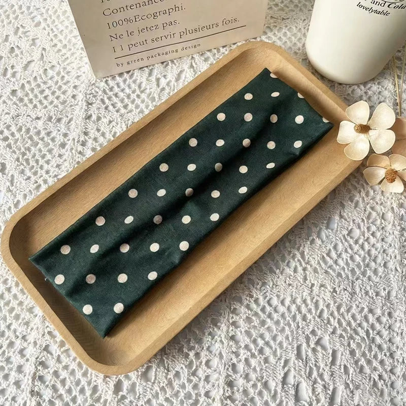 Un bandeau en tissu vert foncé à pois blancs est exposé sur un plateau en bois à côté d'une étiquette.