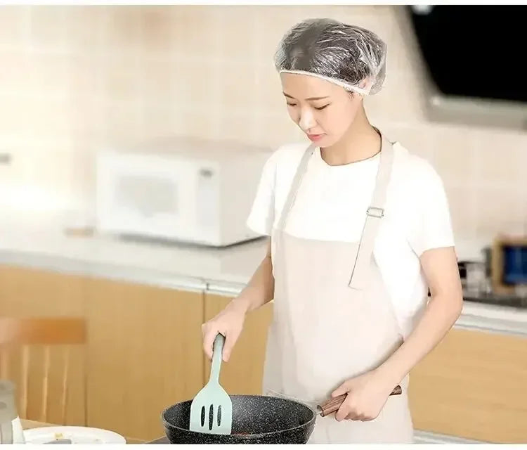 A woman wearing a disposable shower cap is preparing food with a fork in a pan.