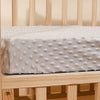Housse de matelas moelleuse et capitonnée blanche pour berceau ou lit pour enfant, posée sur un cadre en bois clair.