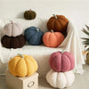 A collection of soft, textured plush pumpkins in various earthy tones like orange, brown, and gray arranged on a white surfac
