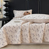 A light beige floral quilted bedspread with a subtle pattern is displayed on a dark headboard.