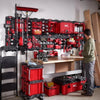 A red and black PACKOUT magnetic bin system mounted on a wall with tools and lumber in a workshop setting.