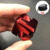 A hand holds a shiny, metallic red fidget cube spinner with a black gift pouch nearby.