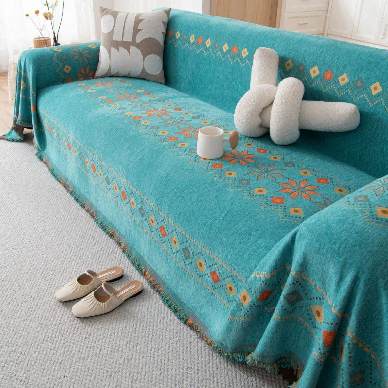 A teal bohemian jacquard sofa cover with orange and white geometric patterns, featuring a white mug and light-colored shoes.