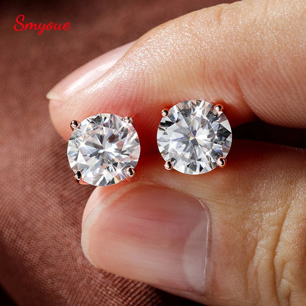 Pendientes tipo stud de moissanita redonda brillante en plata esterlina y baño de oro rosa, puestos en un dedo.