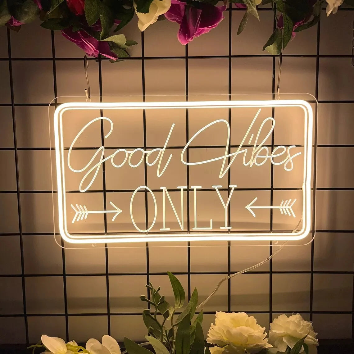 A glowing white LED neon sign with the text Good Vibes ONLY mounted on a black tiled wall.