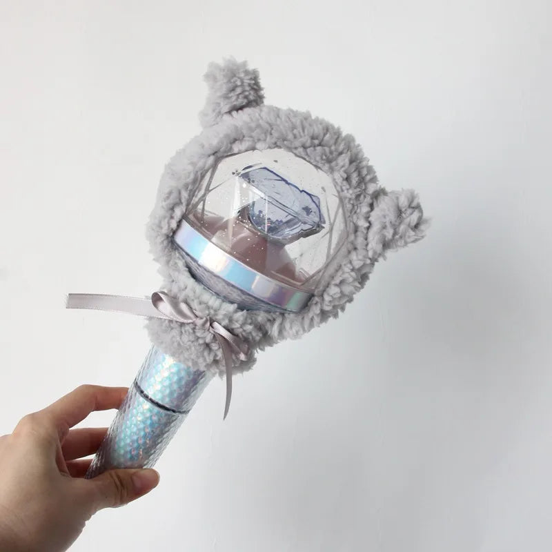 A hand holds a plush, gray, fuzzy cover for a light stick, which is attached to a silver-colored light stick.
