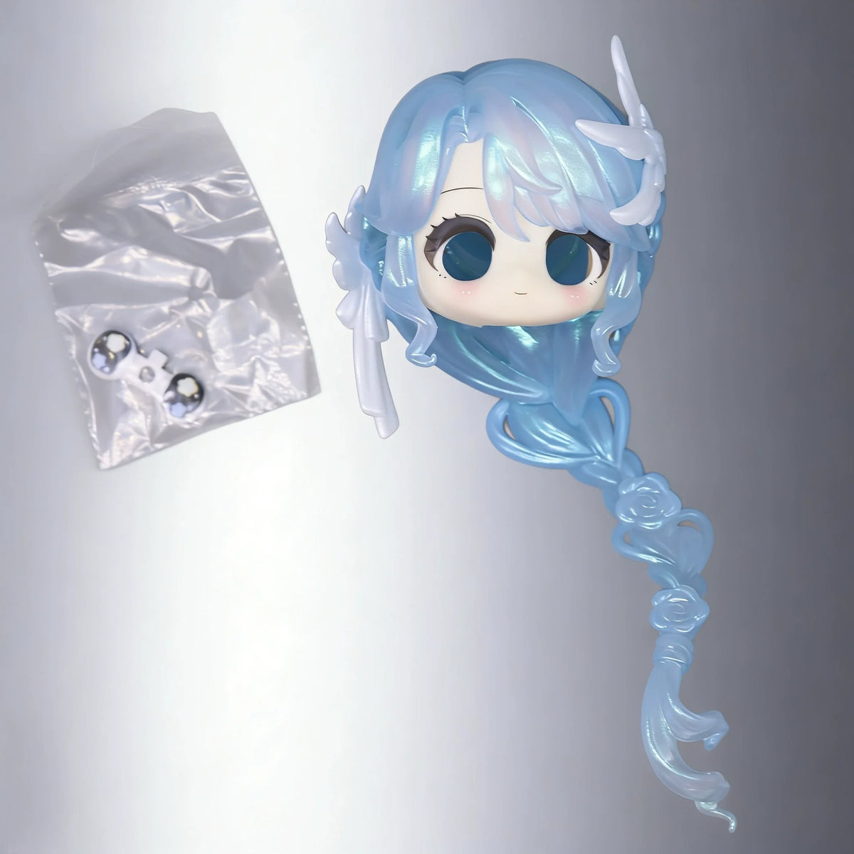 A light blue articulated ball-jointed doll figurine with long hair and translucent wings is shown next to its clear plastic b