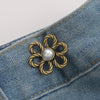 A brass flower-shaped waist clip with a pearl center is attached to a blue denim fabric.