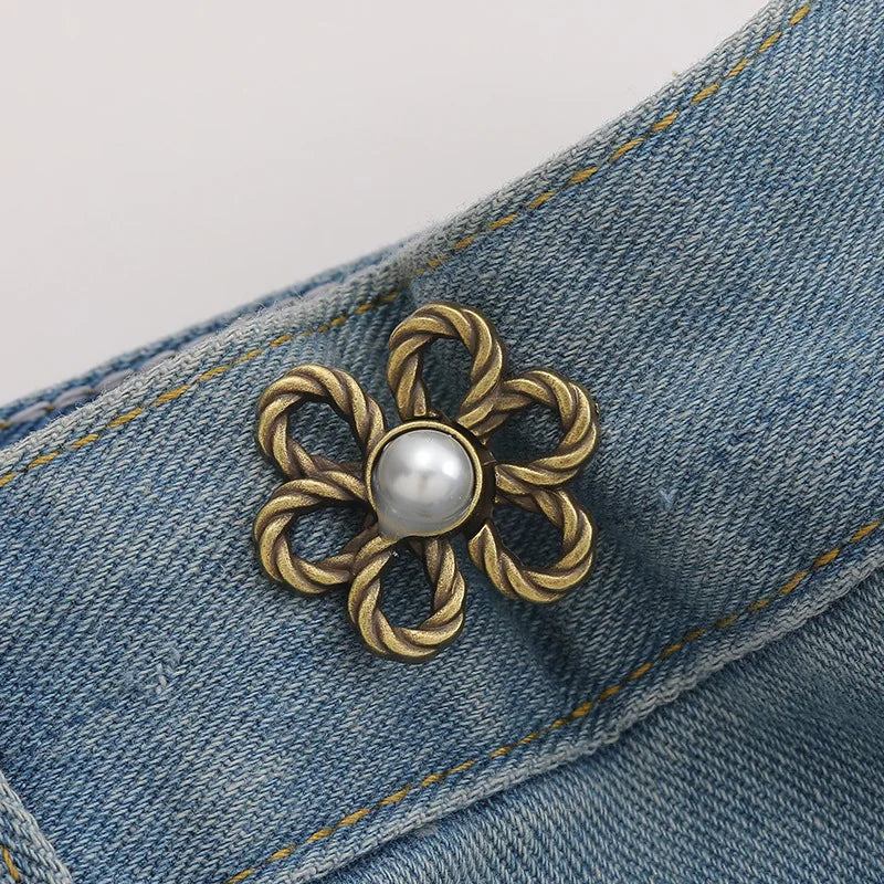 A brass flower-shaped waist clip with a pearl center is attached to a blue denim fabric.