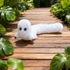 A white plush toy resembling a ghost or creature is lying on a wooden deck surrounded by green foliage.