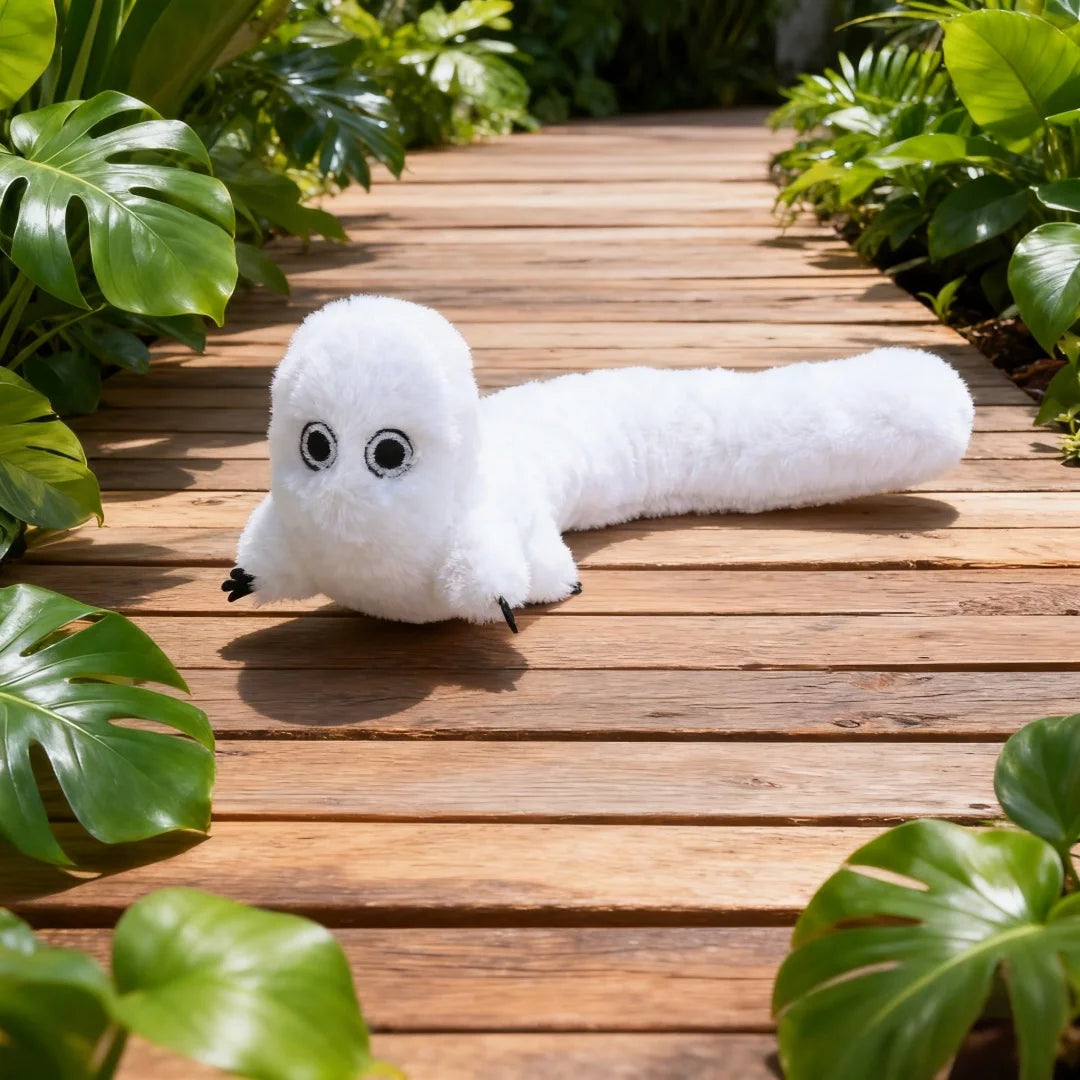 A white plush toy resembling a ghost or creature is lying on a wooden deck surrounded by green foliage.