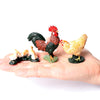 A hand holds three realistic animal figurines: a rooster, a hen, and a chick.