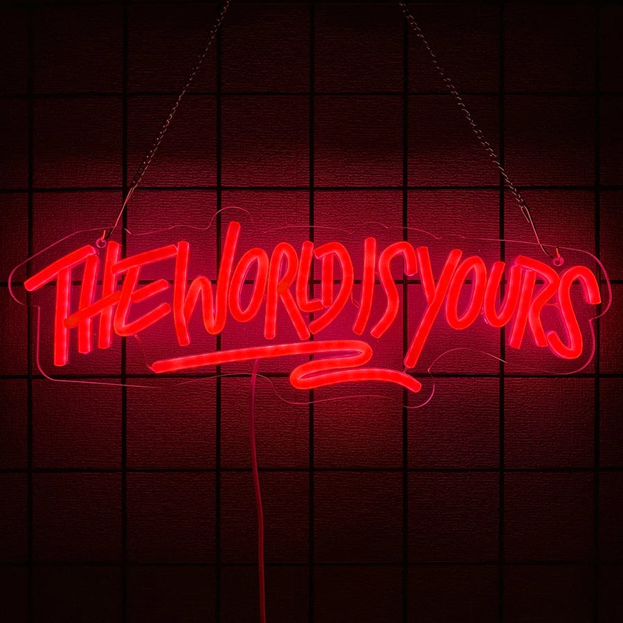 A neon sign spelling out THE WORLD IS YOURS in red light, hanging against a dark grid background.
