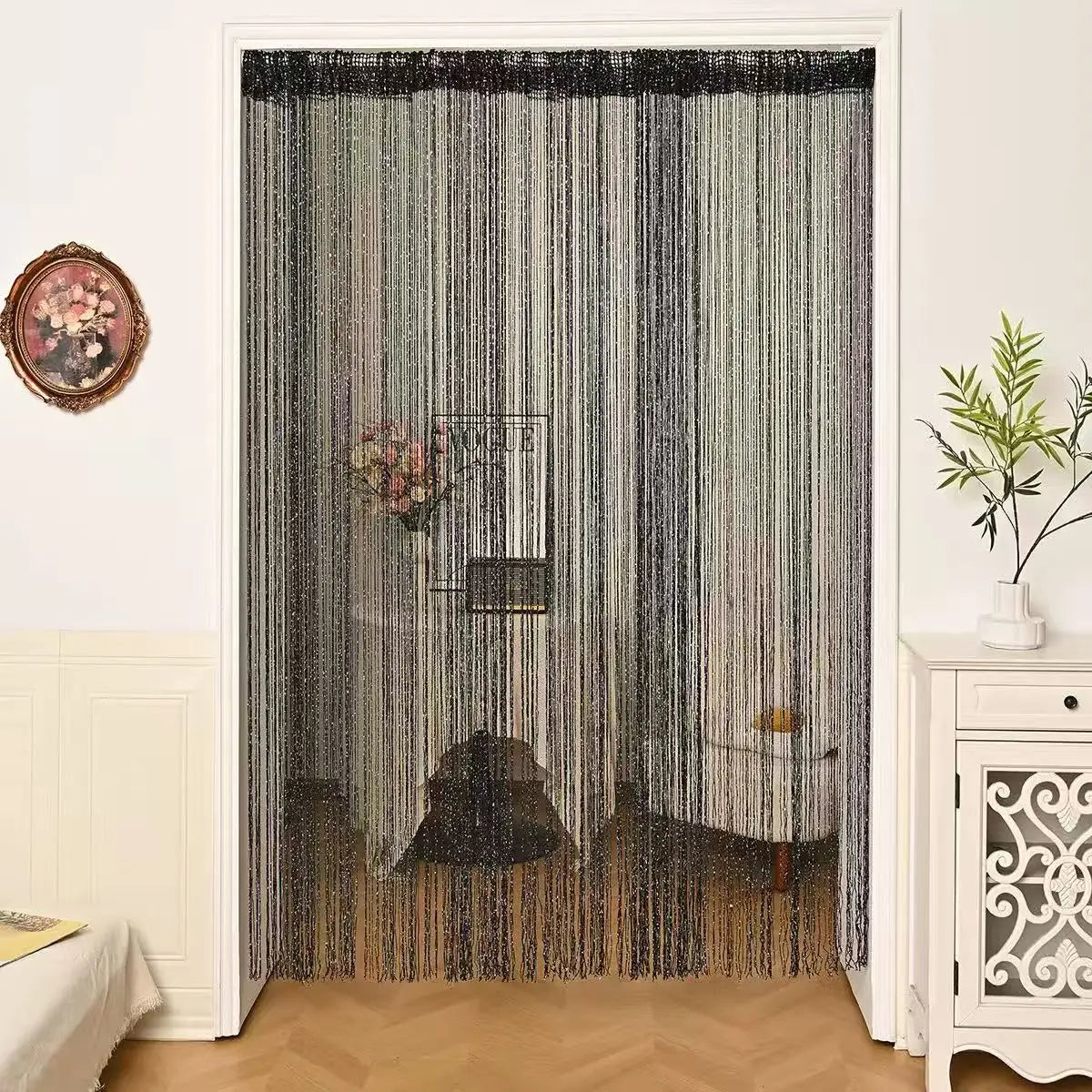 Perlenverzierte Gardinenstange in Grau und Schwarz hängt in einem Türrahmen, dekoriert mit Blumenarrangements.
