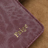 A deep plum colored leather passport holder with gold embossed name on a textured brown background.