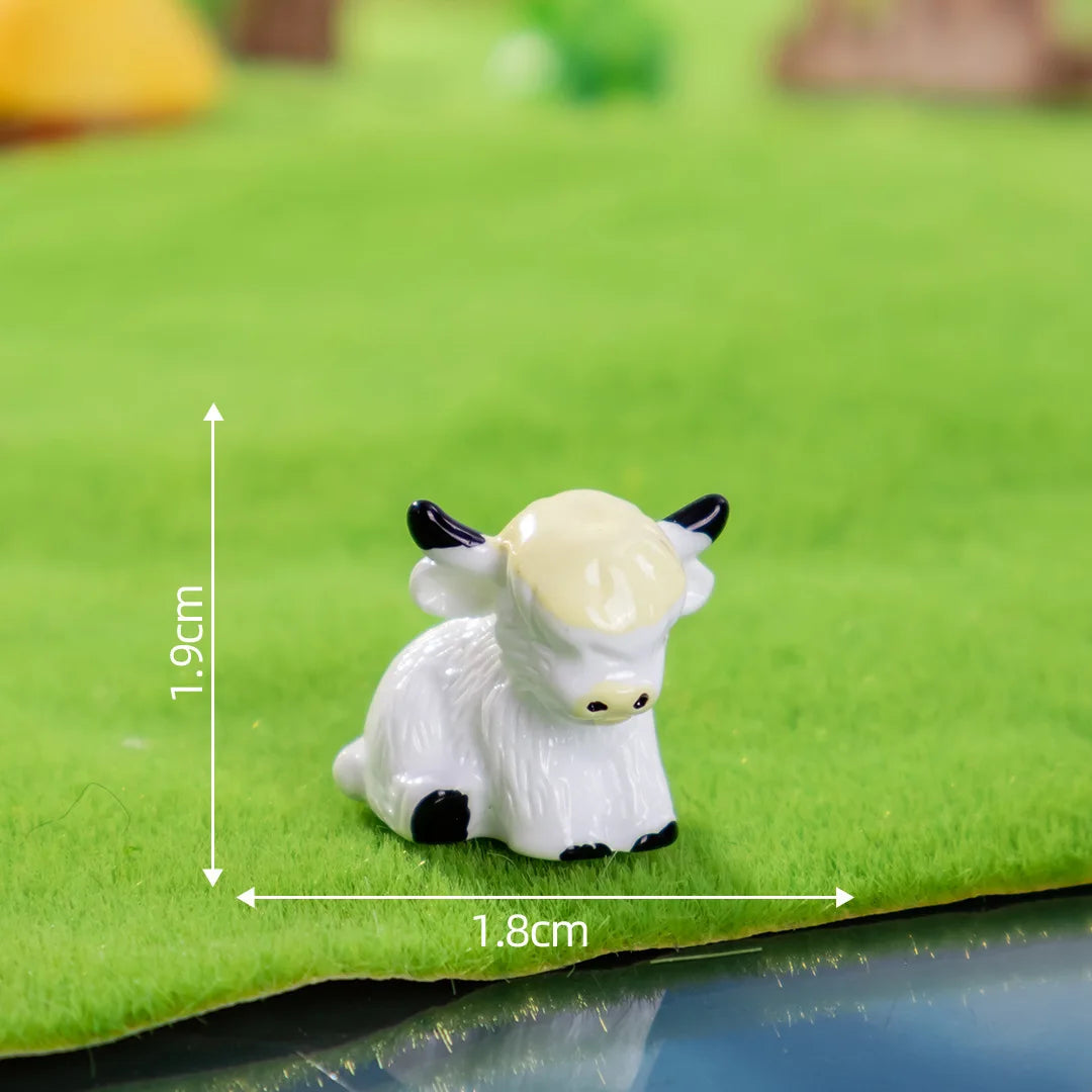A small white resin Highland cow figurine standing on green grass.