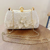 A white pearl embroidered evening clutch with a gold chain strap resting on a wooden surface.
