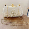 A white pearl embroidered evening clutch with a gold chain strap resting on a wooden surface.