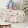 A quilted cosmetic pouch in white with a vintage rose print and pink lace trim, resting on a light surface.