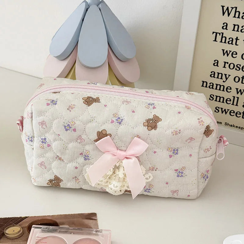 A quilted cosmetic pouch in white with a vintage rose print and pink lace trim, resting on a light surface.