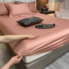 Primer plano de un juego de sábanas rosas ajustadas con almohadas y una piedra decorativa oscura sobre la superficie.