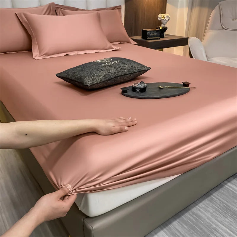 Primer plano de un juego de sábanas rosas ajustadas con almohadas y una piedra decorativa oscura sobre la superficie.