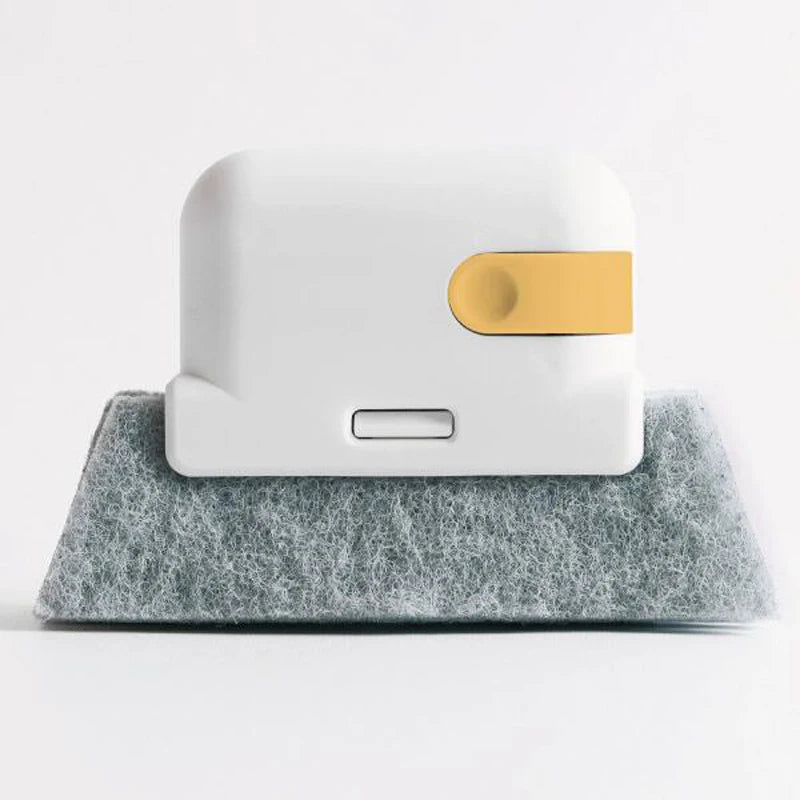 A white multi-surface gap cleaning brush with a gold scouring pad resting on a gray felt surface.