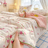 A hand is holding a pink floral quilt blanket with a soft washed finish on a bed.