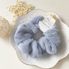 A pair of soft, light blue plush coil hair ties resting on a white plate with gold rim.