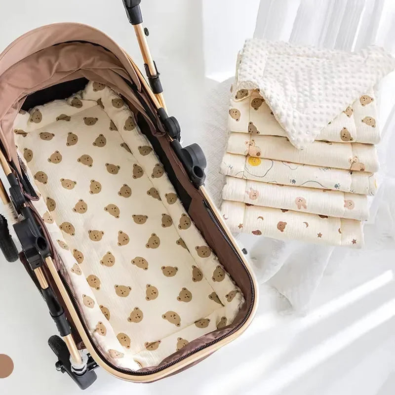 A beige and brown cozy cartoon bear stroller cushion is shown next to a stack of cream-colored fabric items.