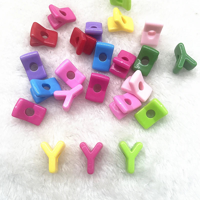 A collection of 10 mixed colored alphabet letter beads scattered on a white surface.