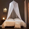 A sheer white ceiling-hung dome mosquito net draped over a bed in a dimly lit room.