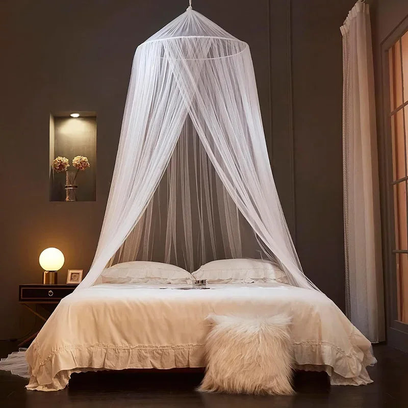 A sheer white ceiling-hung dome mosquito net draped over a bed in a dimly lit room.