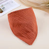 A terracotta orange soft cotton baby bib with a ribbed texture lying on a light surface.