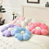 A collection of plush daisy flower throw pillows in shades of pink, purple, and blue resting on a white bed.