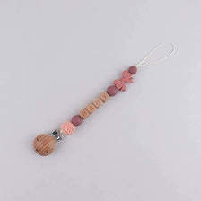A beaded silicone pacifier clip lanyard featuring a pink bow and wooden name beads.