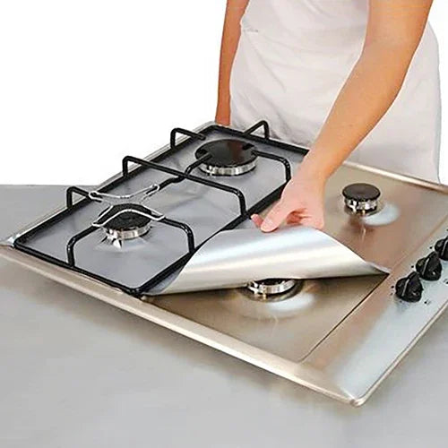 A person is placing a reusable square gas hob protector liner onto a stainless steel cooktop.