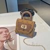 A small, tan floral textured crossbody tote bag with a gold chain resting on a white surface.