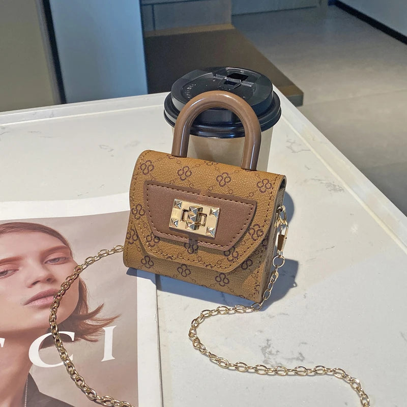 A small, tan floral textured crossbody tote bag with a gold chain resting on a white surface.