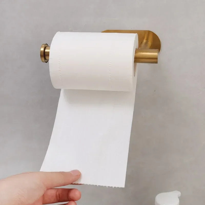 A hand holds a roll of white toilet paper on a stainless steel self-adhesive holder against a light gray background.