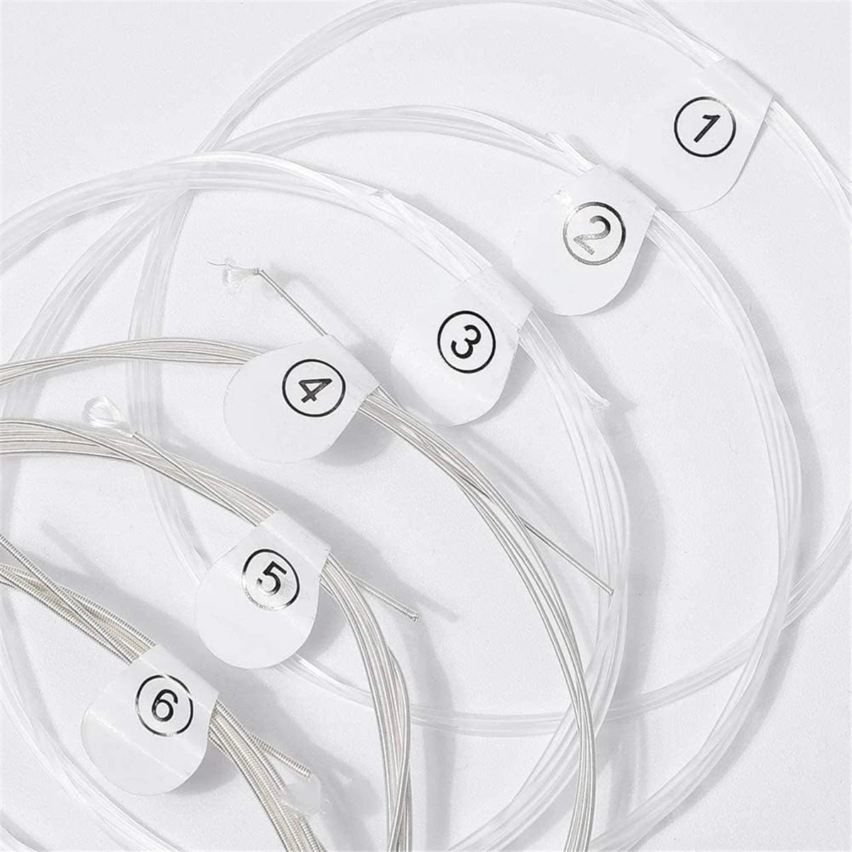 A collection of six silver-plated nylon guitar strings are laid out on a white surface, numbered one through six.