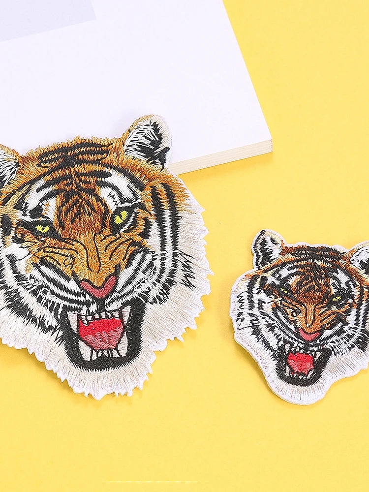 A detailed embroidery patch featuring a fierce tiger head with yellow eyes and striped fur on a yellow background.